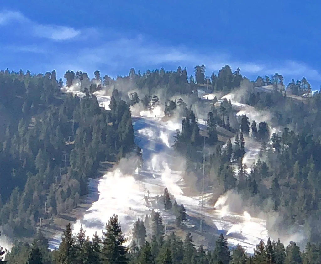 Snowmaking machines operating on a ski slope at Big Bear, California under a clear blue sky.