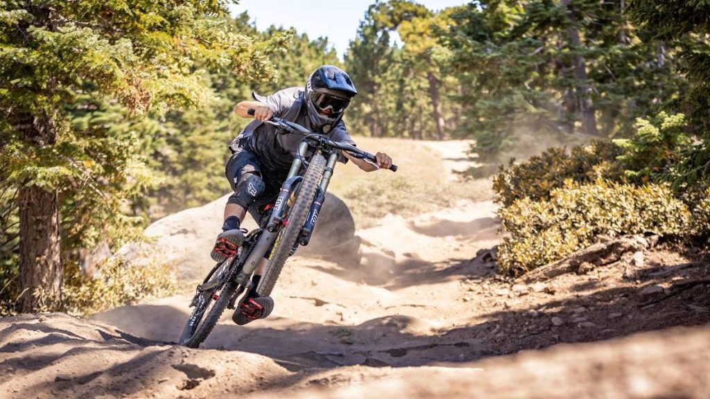A person riding a mountain bike down a rocky, dusty trail through trees.