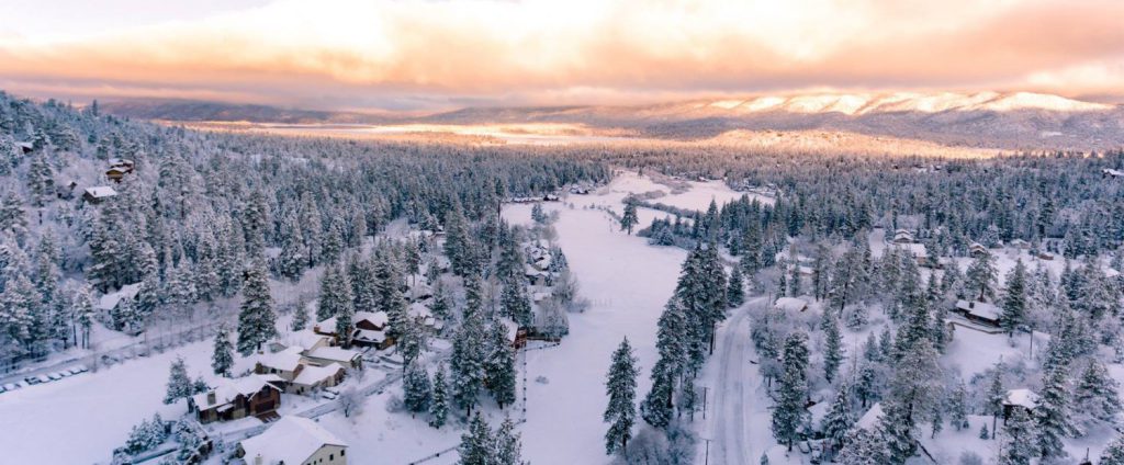 Aerial winter view of Big Bear neighborhood surrounded by snow-covered forest