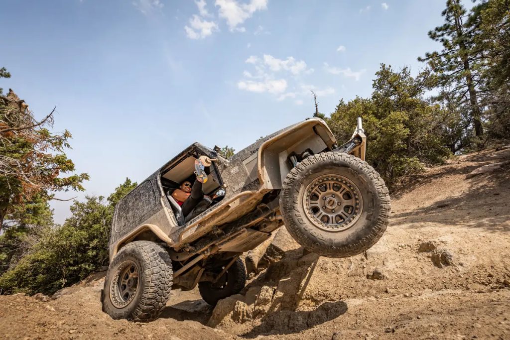 A jeep climbing a rocky trail in an off-road adventure, with a person hanging out of the vehicle.