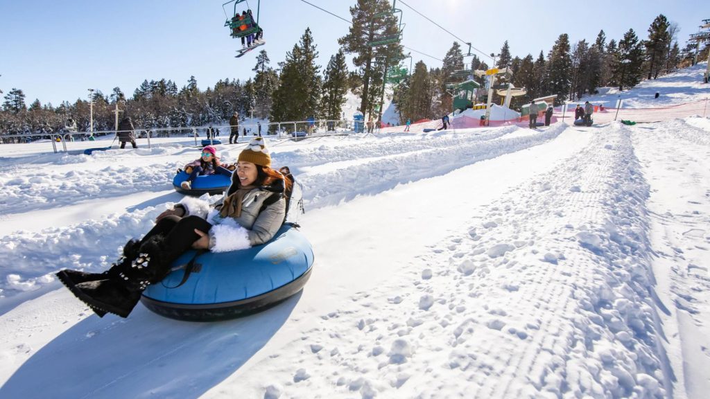 People enjoying snow tubing down a snowy hill with a ski lift in the background.