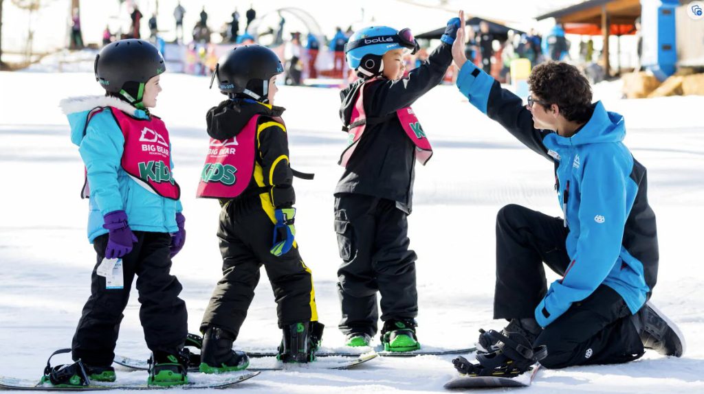 A group of children in snowboarding gear, learning from an instructor while enjoying the snow at Big Bear.