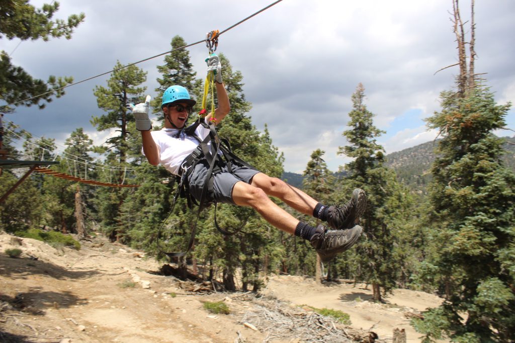A person enjoying a thrilling zipline ride through the trees with a big smile, wearing a helmet and harness.