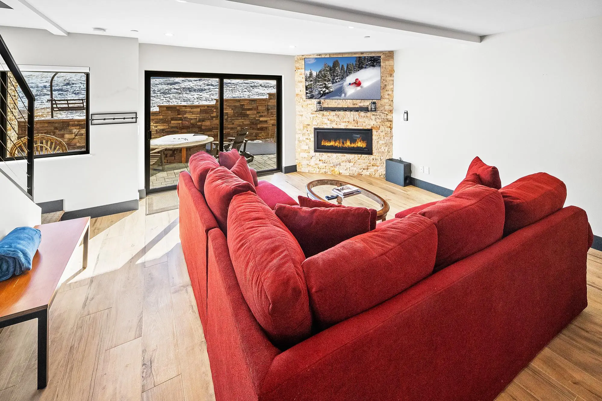 Living room with red sectional, fireplace, TV showing snowy scene, and glass doors to patio with hot tub.