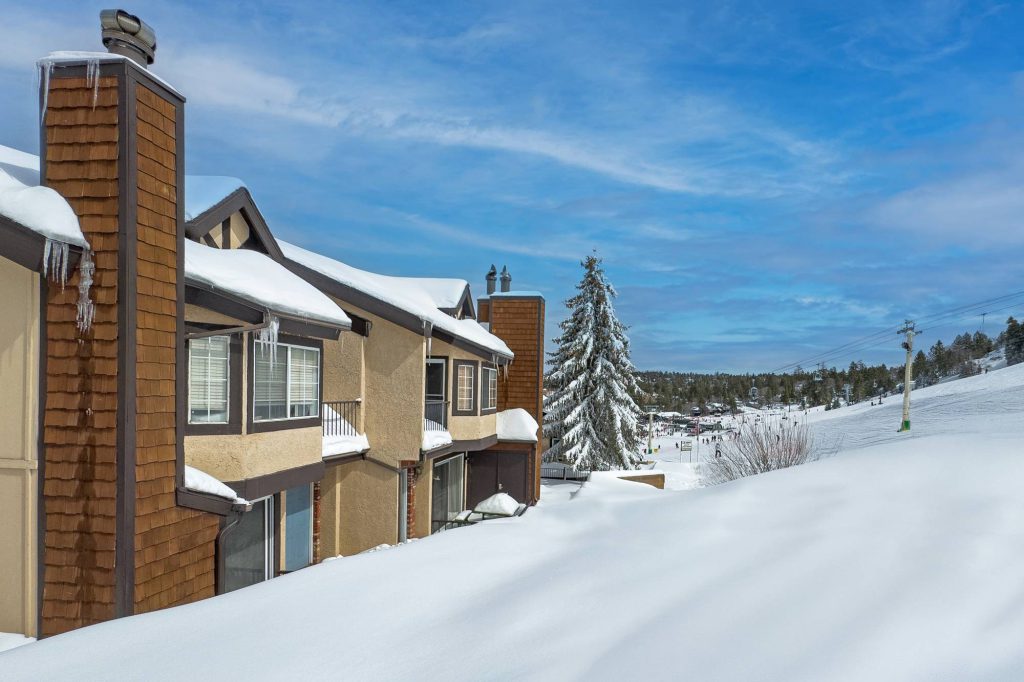 Snow-covered condo exterior with chimney and ski slope in background