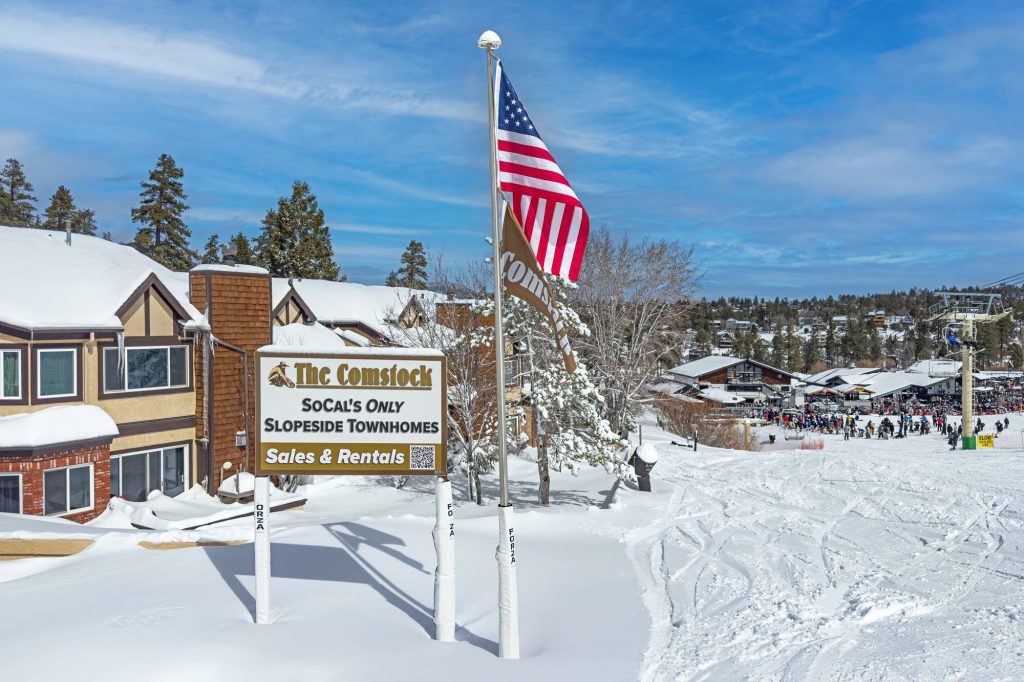 The Comstock slopeside townhomes sign and American flag overlooking ski slopes in Big Bear Lake